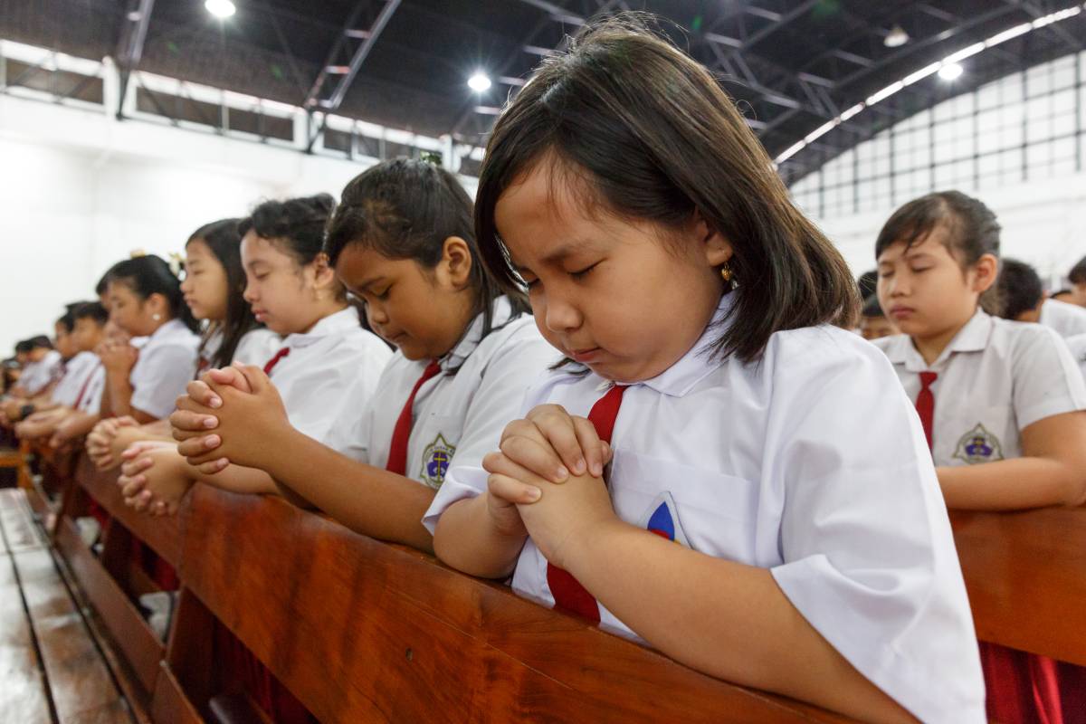 Group of Indonesian kids bowed in prayer at a church pew.